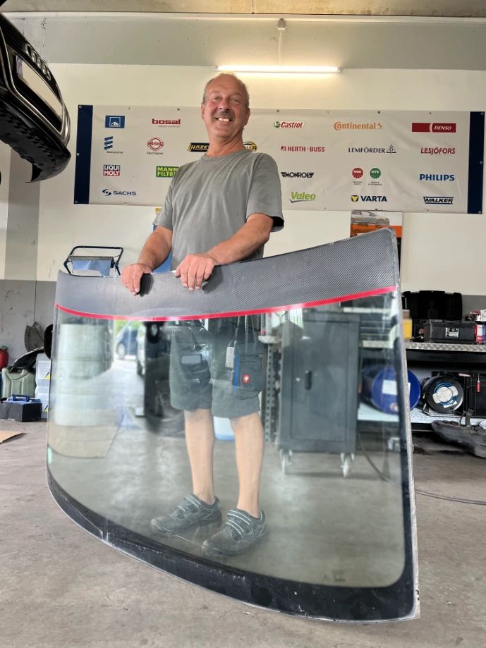Dirk Menzel mit einer ausgebauten Windschutzscheibe in der Werkstatt